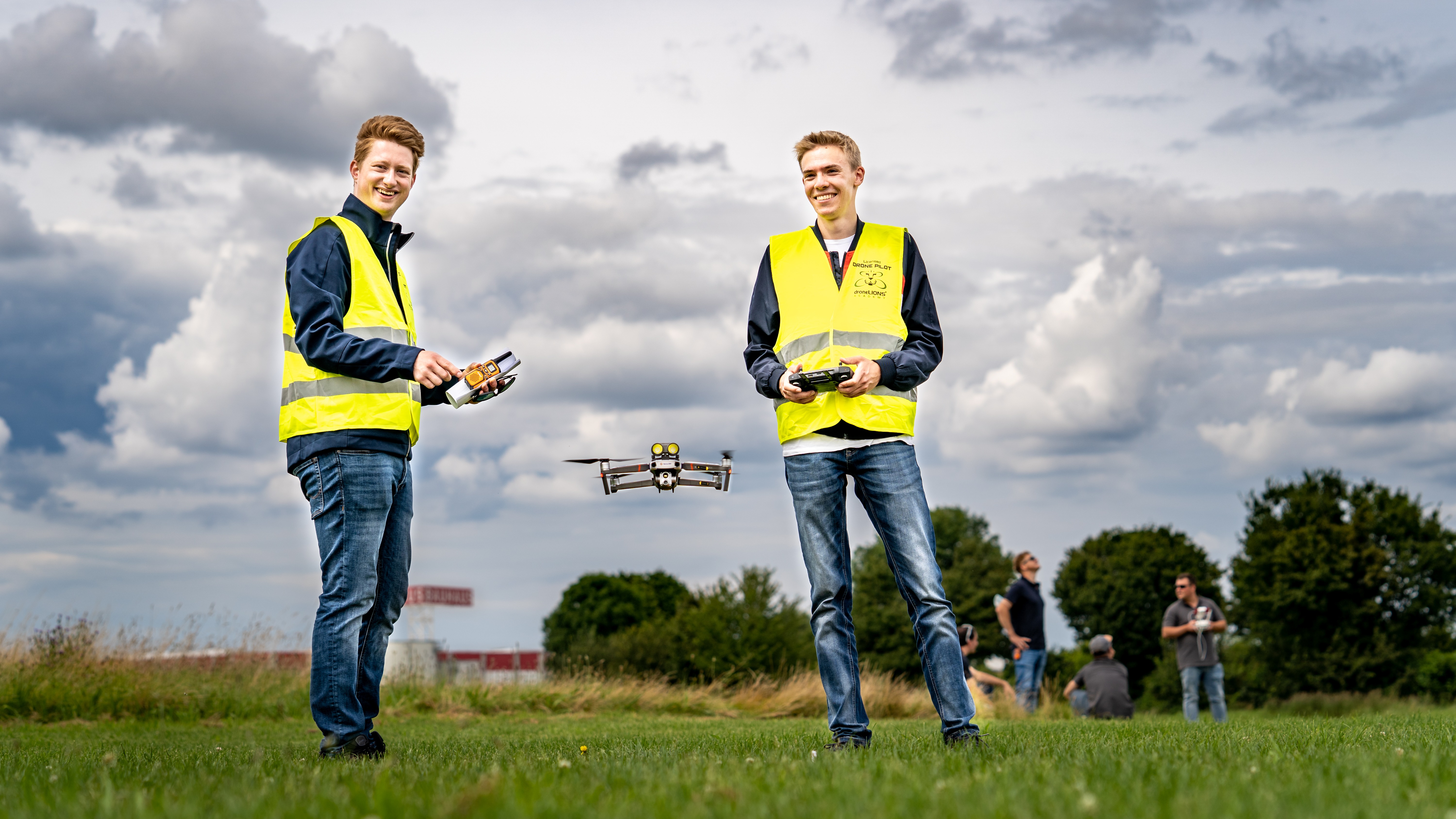 Zwei junge Männer mit gelben Warnwesten steuern eine Drohne.