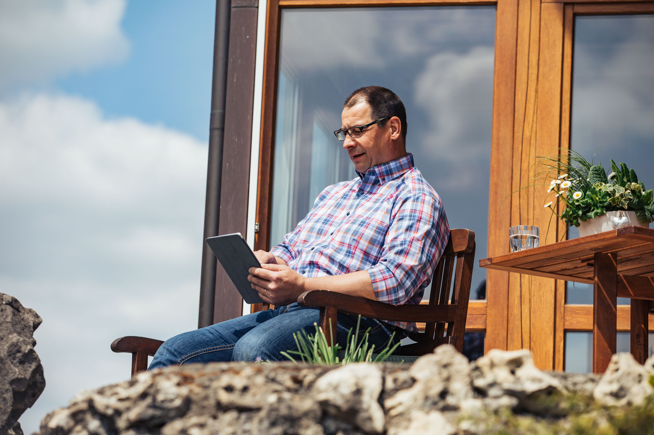 Mann sitzt vorm Haus und guckt auf sein Tablet.