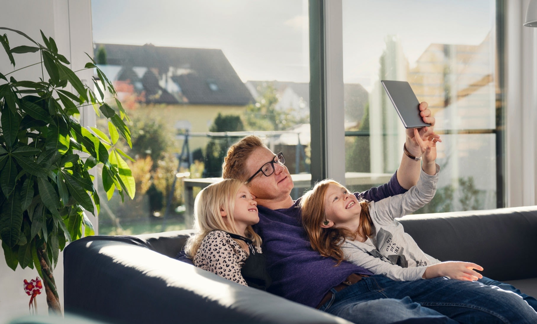 Vater mit zwei Töchtern auf Sofa, Tablet in der Hand.