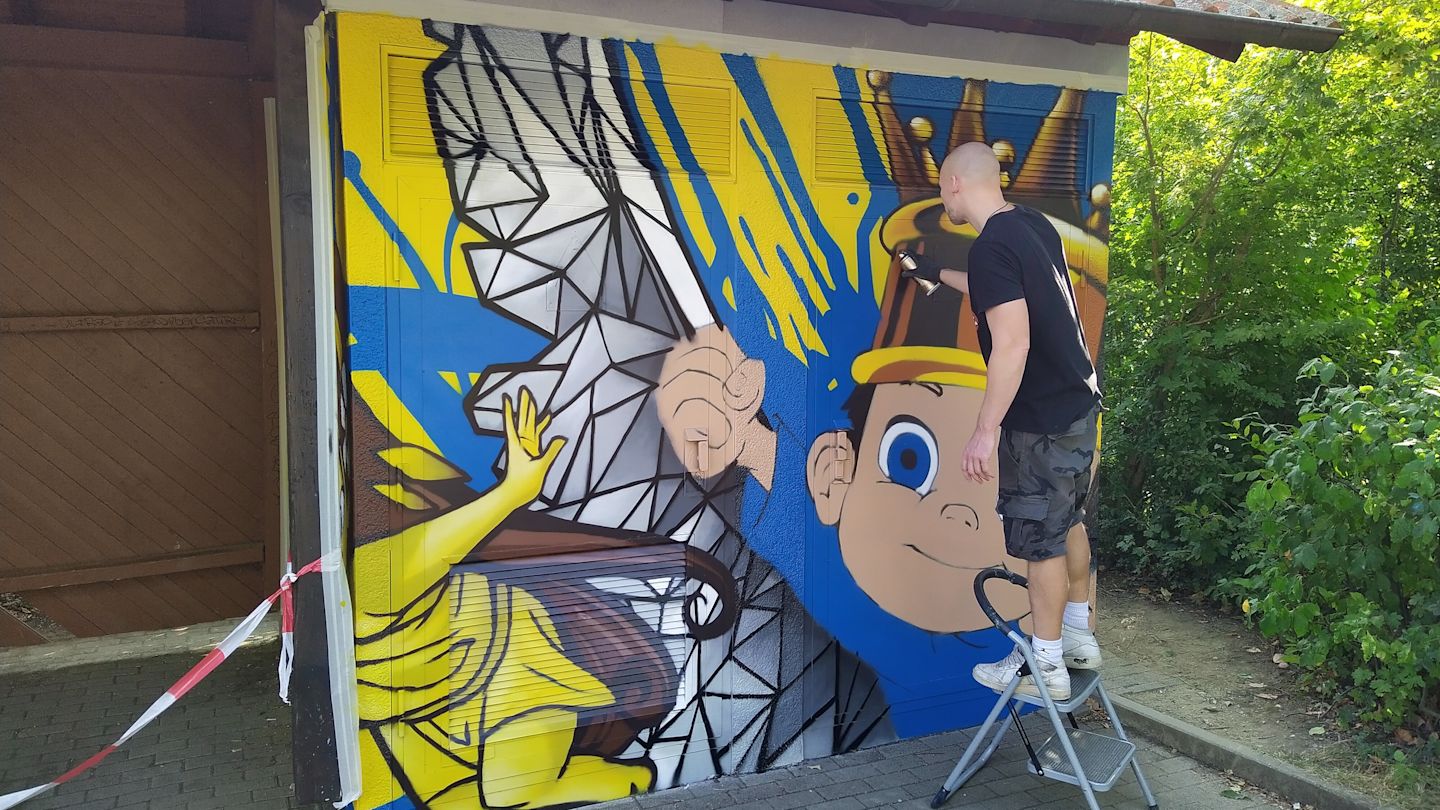 Graffiti-Künstler malt farbenfrohes Wandbild von kleinem Jungen mit Krone.