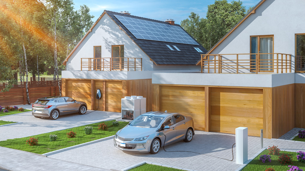 Zwei E-Autos laden vor einem Haus mit Solaranlage.