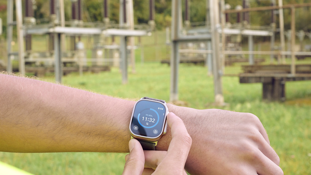 Smartwatch zeigt Countdown vor Hochspannungsanlage.