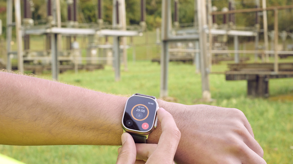 Smartwatch zeigt Countdown vor Hochspannungsanlage.