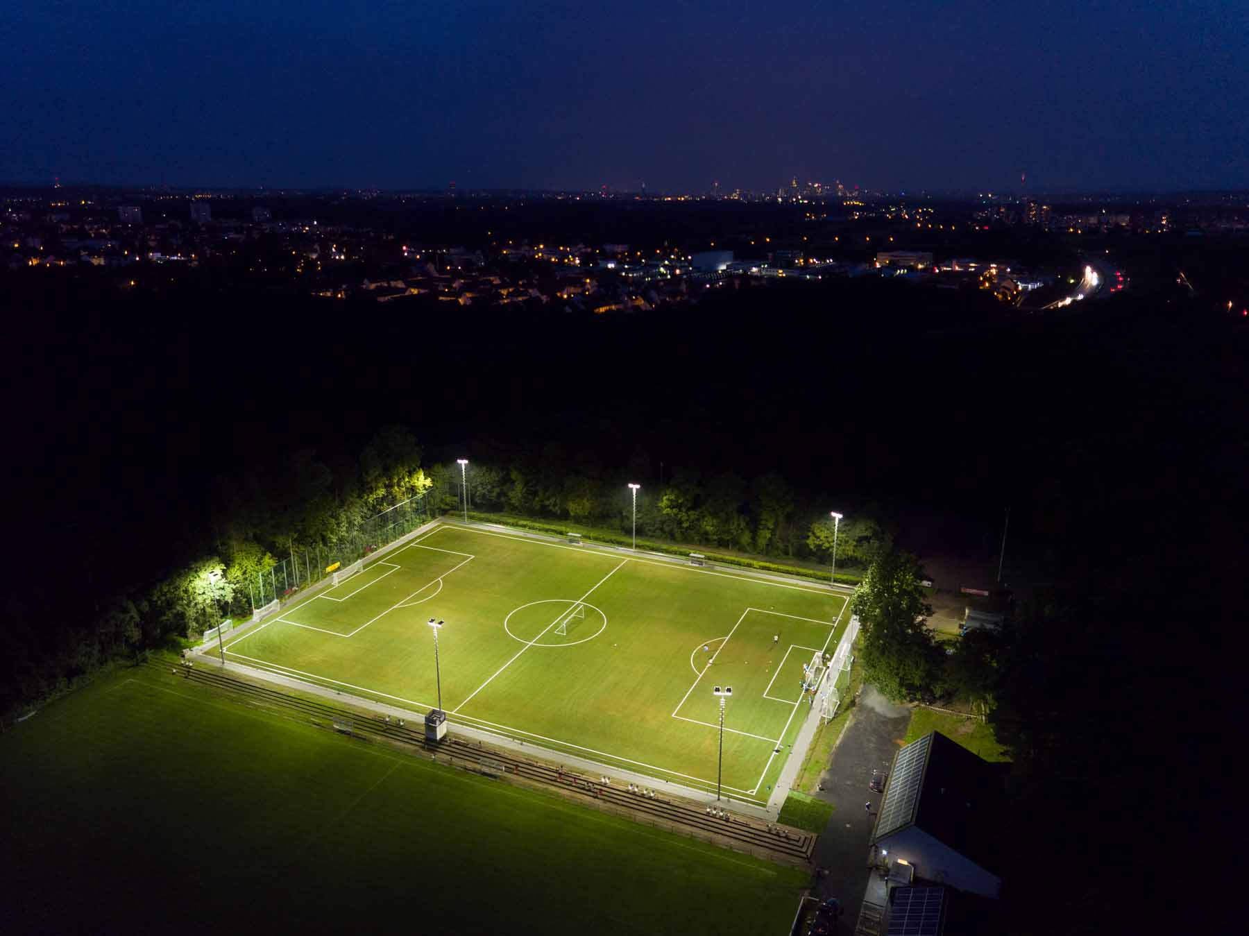 Beleuchteter Fußballplatz bei Nacht von oben.