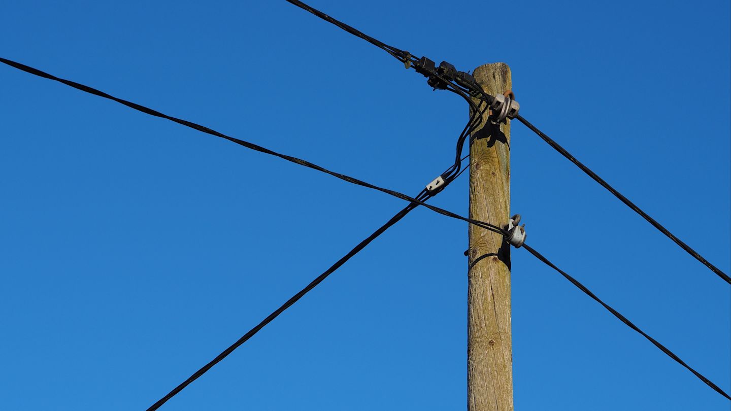 Holzpfahl mit Stromkabeln vor blauem Himmel.