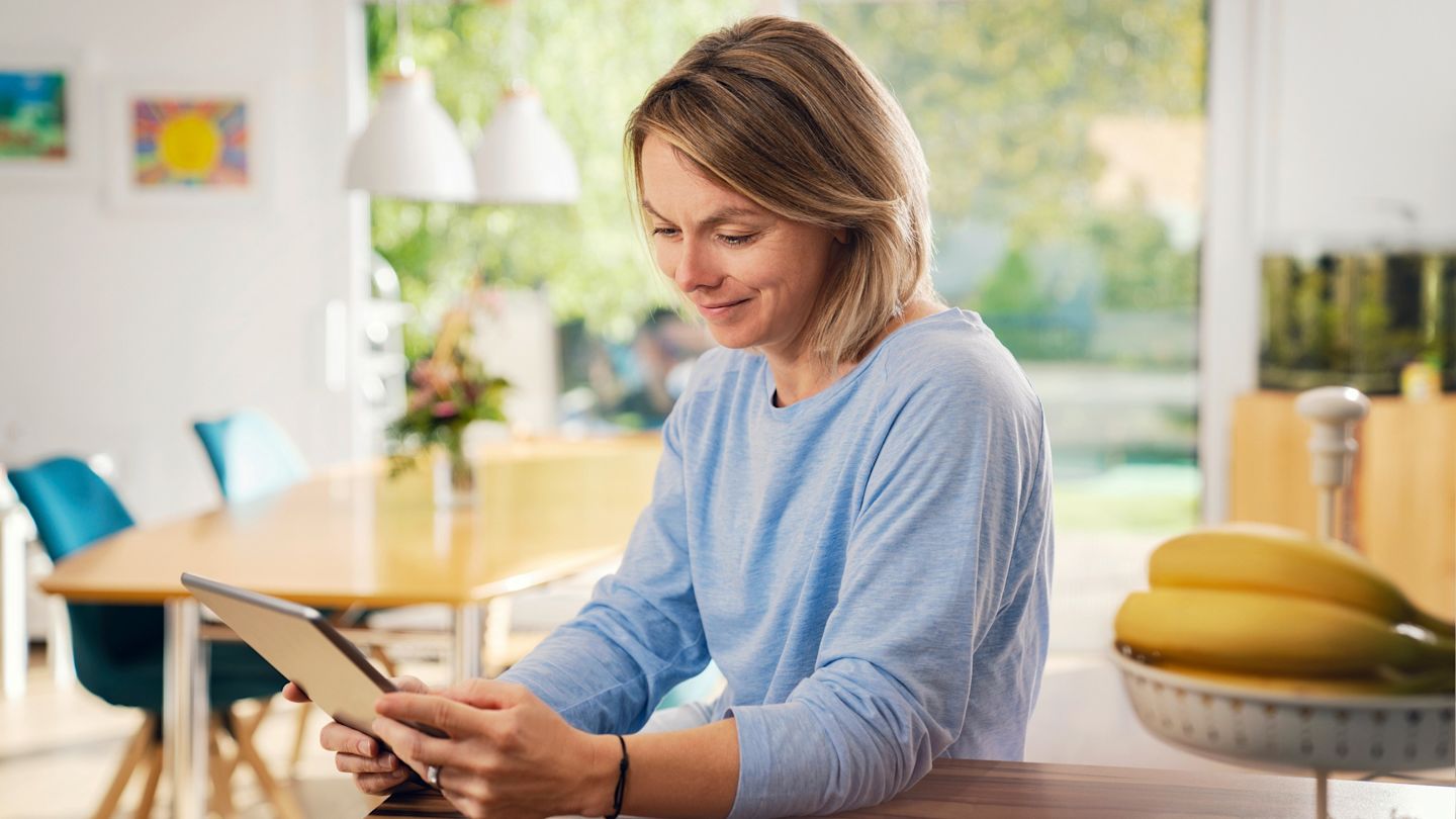 Lächelnde Frau benutzt Tablet in heller Küche.