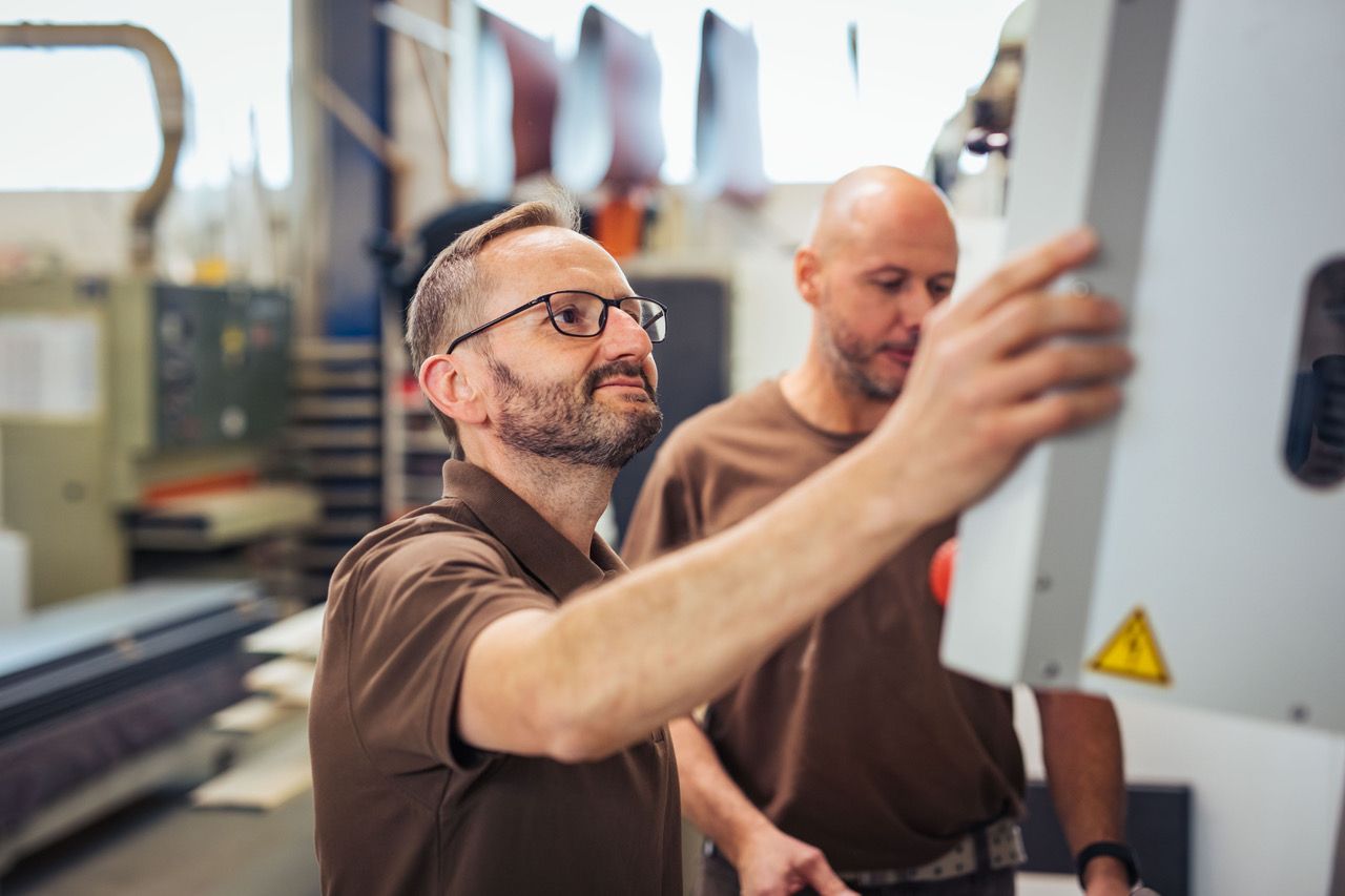 Zwei Männer bedienen eine Maschine in einer Werkstatt.