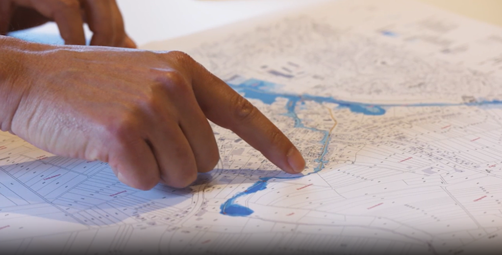 Hand zeigt auf Überschwemmungsgebiet auf Karte.