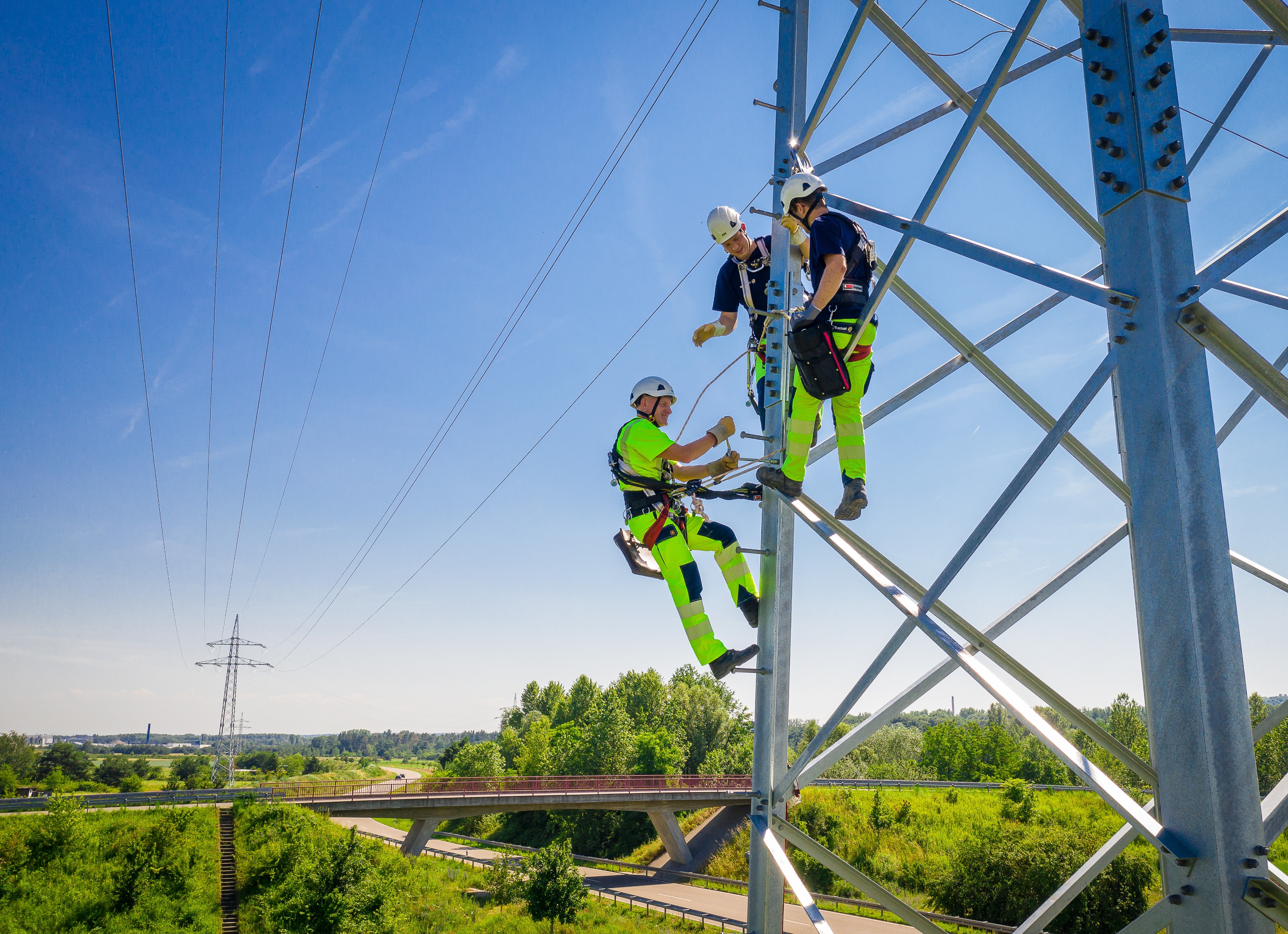 Drei Monteure arbeiten an einem Hochspannungsmast.