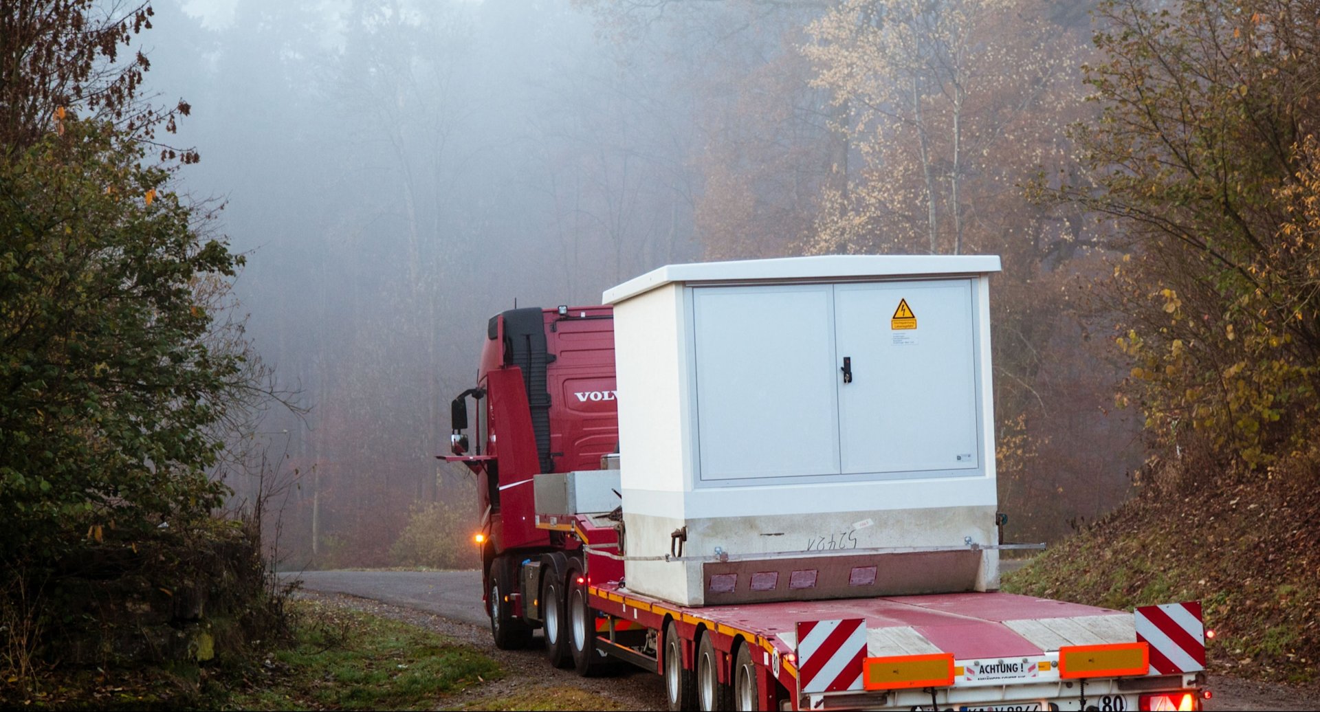 LKW transportiert weiße Trafostation.