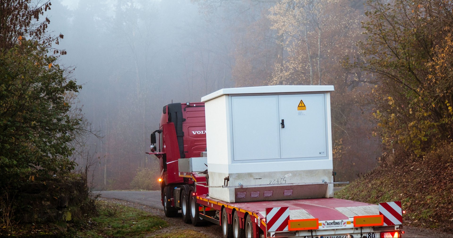 LKW transportiert weiße Transformatorenstation.