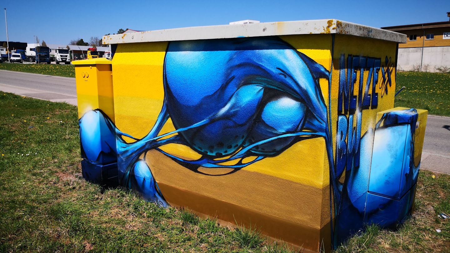 Gelber Stromkasten mit blauem Graffiti.