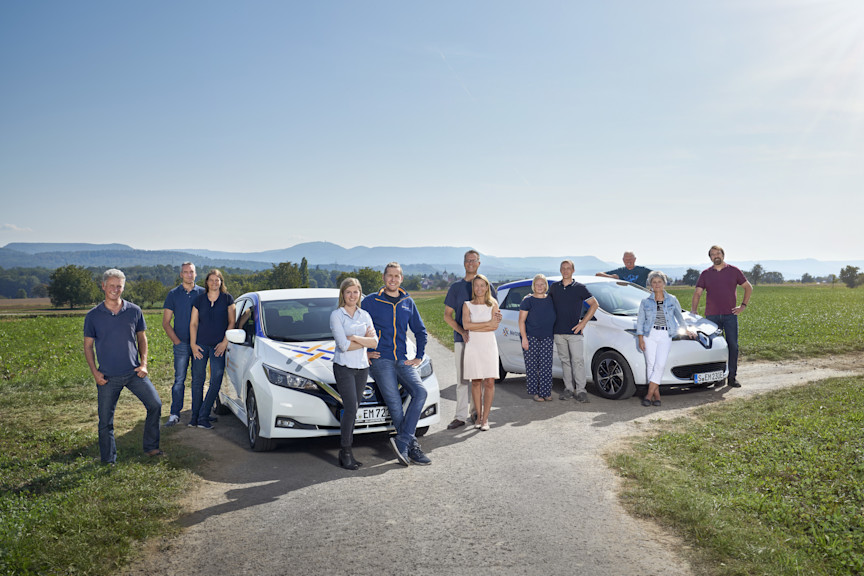 Eine Gruppe von Menschen neben zwei weißen E-Autos vor einem Feld.