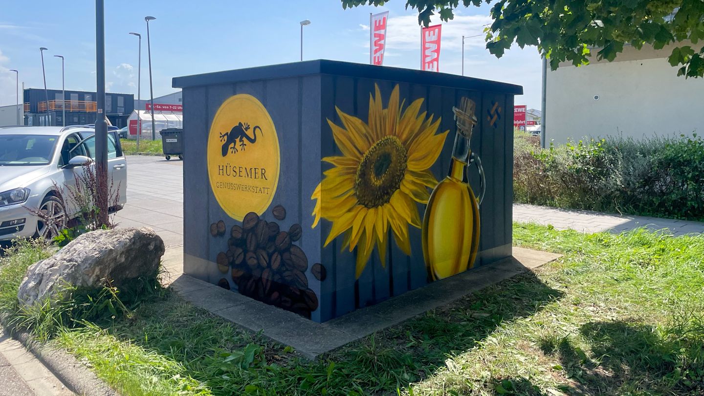 Graffiti auf Kasten: Sonnenblume, Kaffee und Logo.
