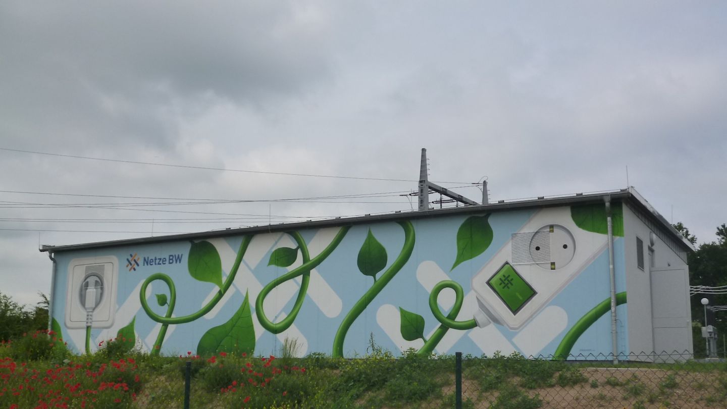 Gebäude mit Wandgemälde: grüne Ranken, Steckdose, Netze BW Logo.