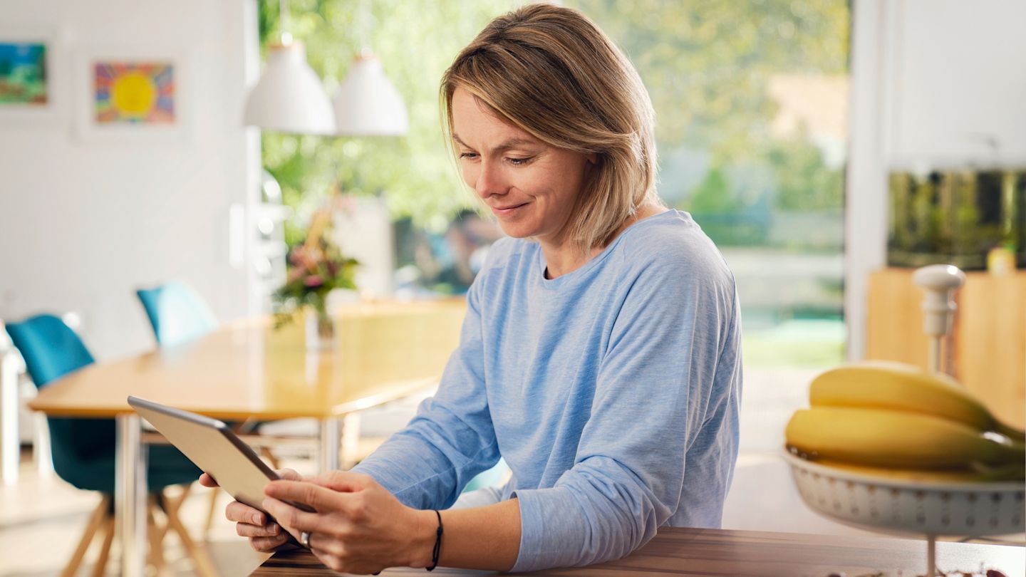 Frau benutzt Tablet am Küchentisch.
