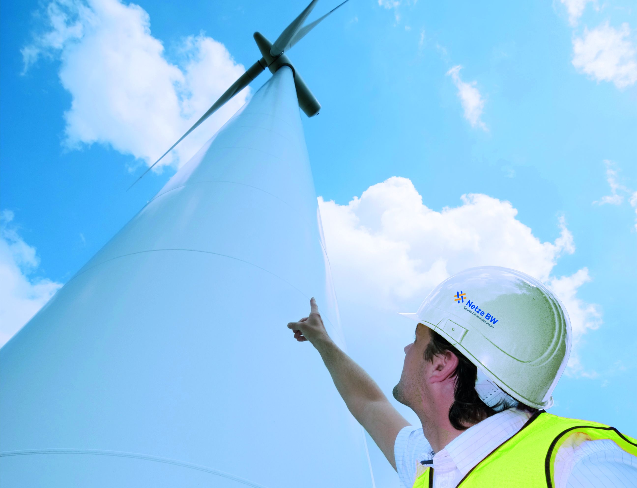 Arbeiter zeigt von unten auf Windkraftanlage.