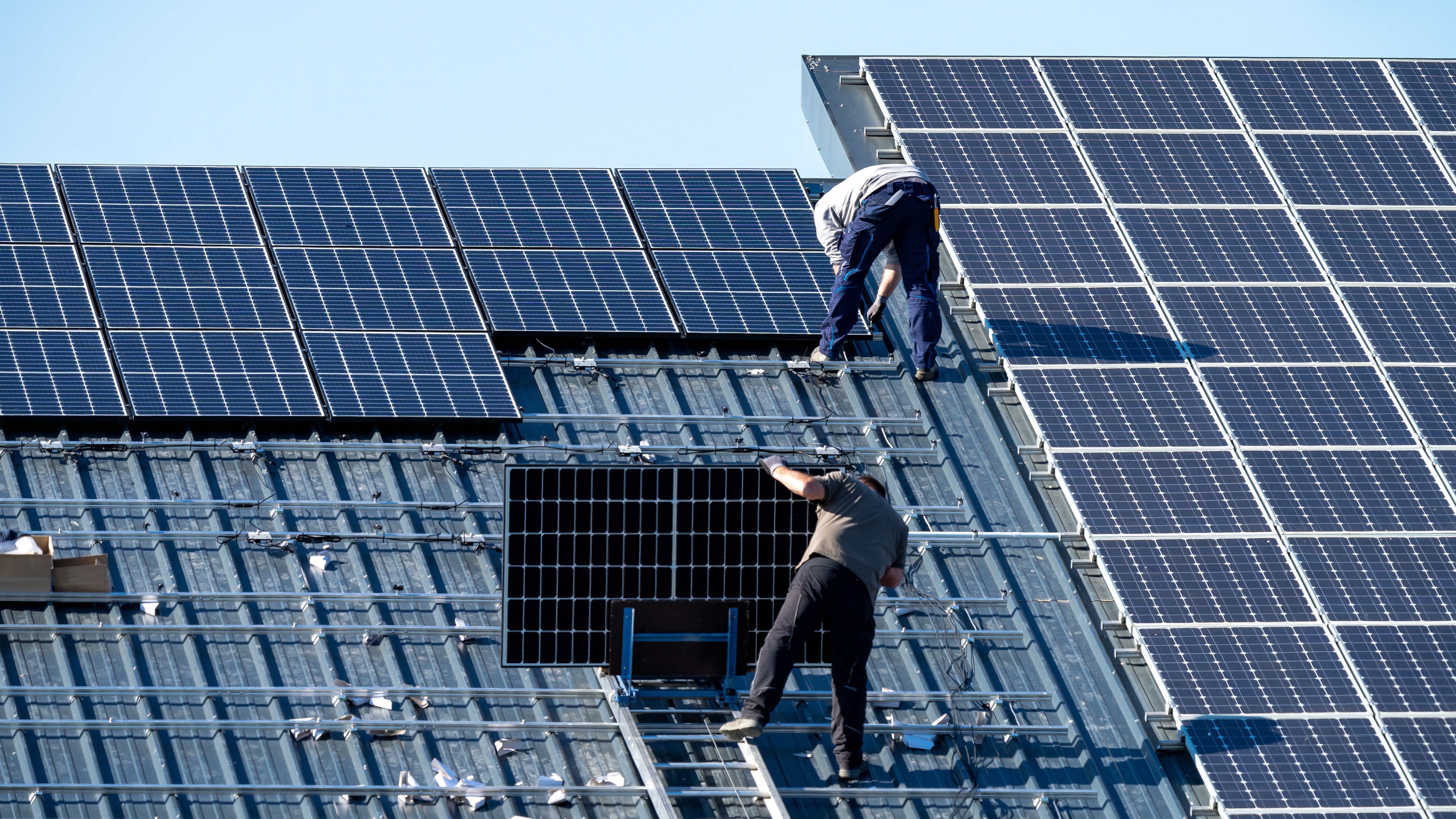 Zwei Arbeiter montieren Solarmodule auf einem Dach.