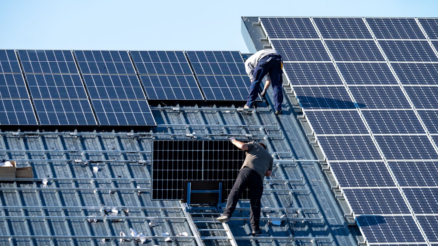 Zwei Arbeiter montieren Solarmodule auf einem Dach.