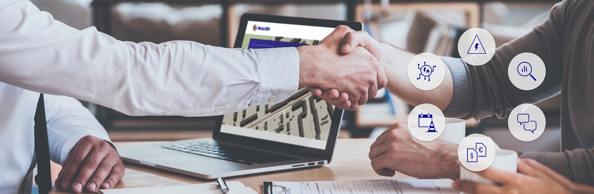 Zwei Männer geben sich die Hand vor einem Laptop.