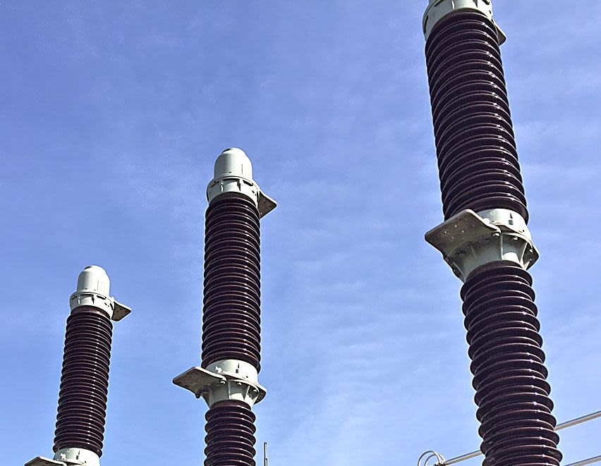 Drei Hochspannungsisolatoren vor blauem Himmel.