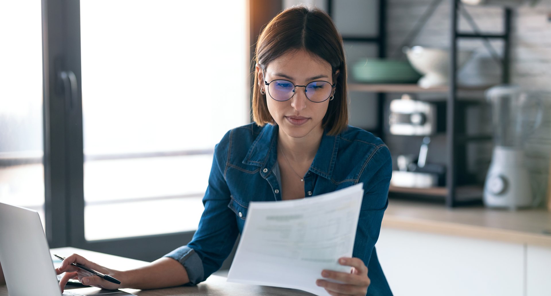Frau liest Dokumente am Laptop.