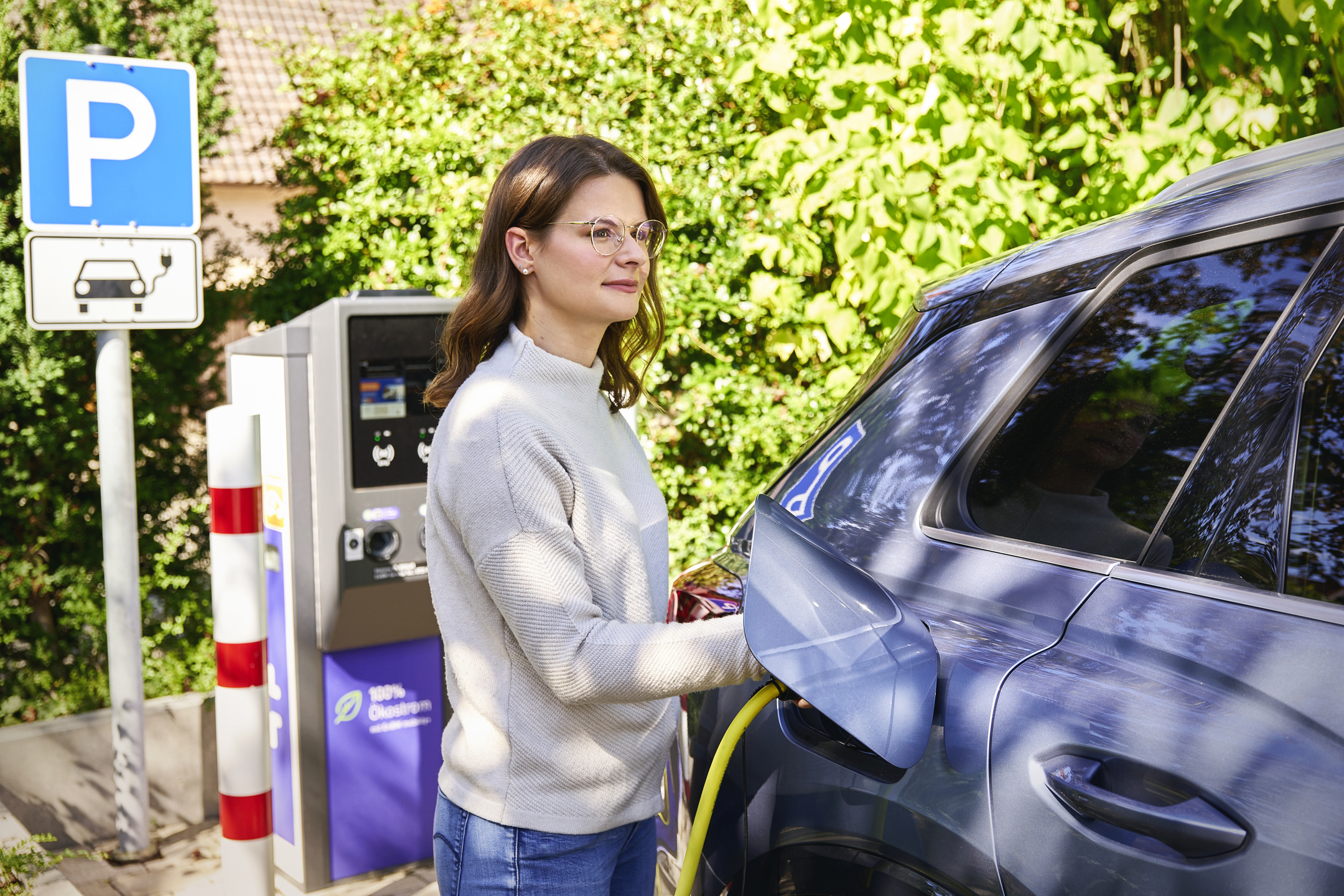 Frau lädt E-Auto an Ladesäule.