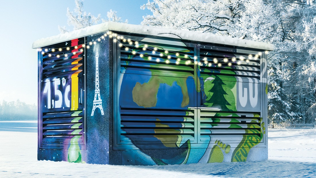 Buntes Trafohäuschen im Schnee mit festlicher Beleuchtung.