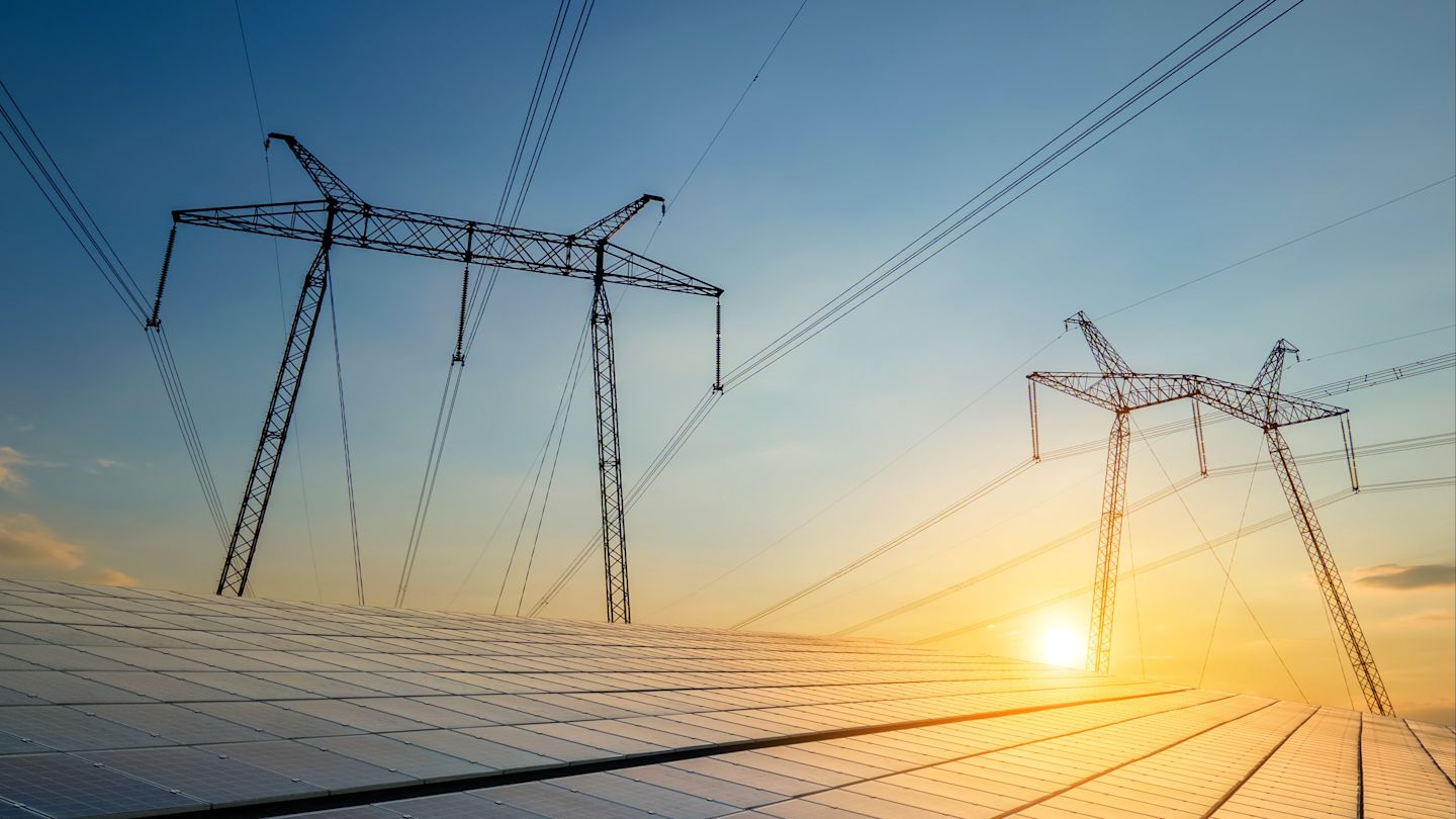 Solaranlage mit Hochspannungsmasten bei Sonnenuntergang.
