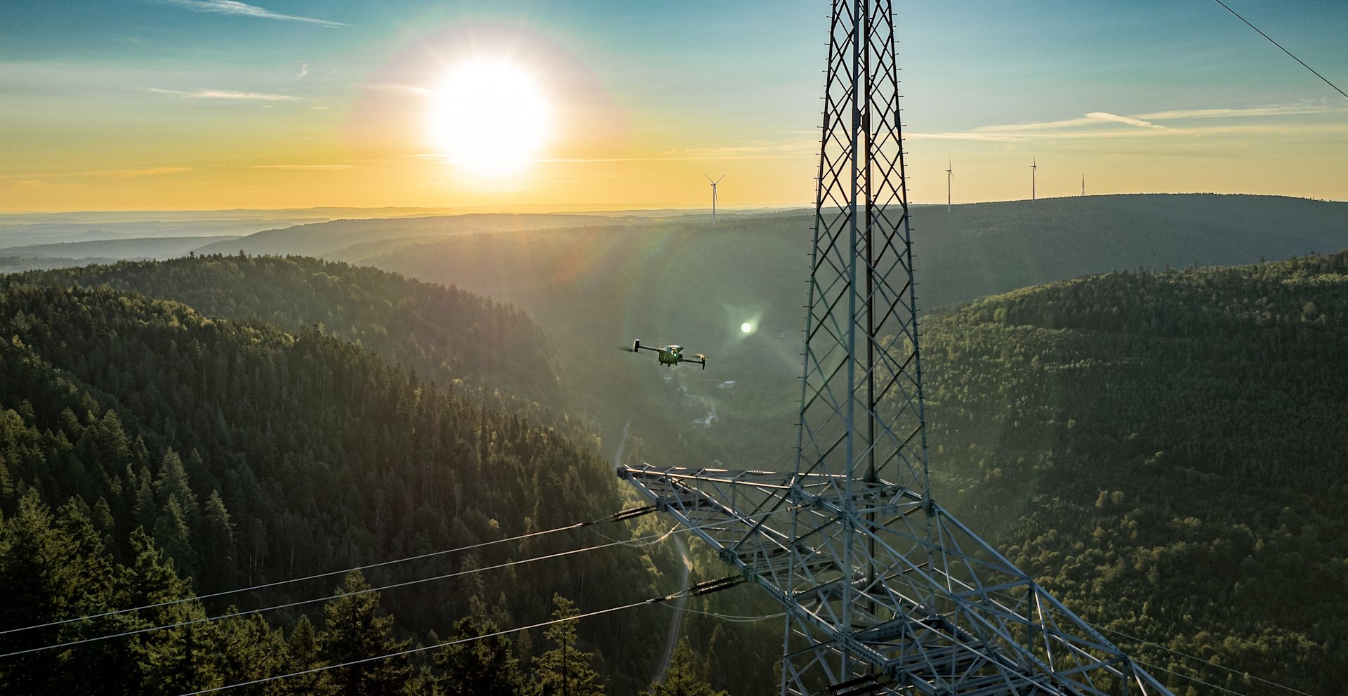 Drohne inspiziert Hochspannungsleitungen bei Sonnenuntergang.