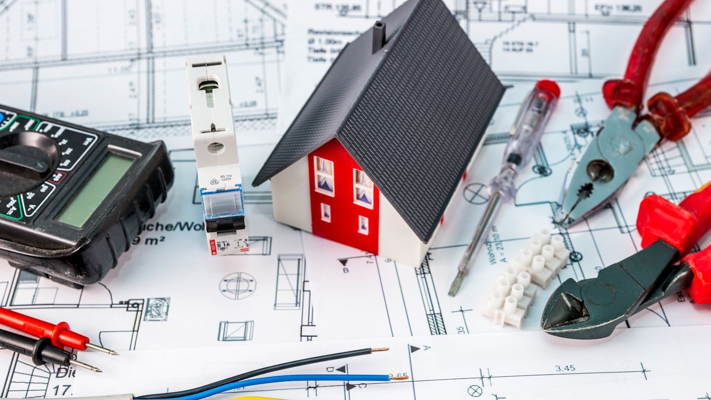 Hausplan, Modellhaus und Zangen liegen auf einem Tisch.