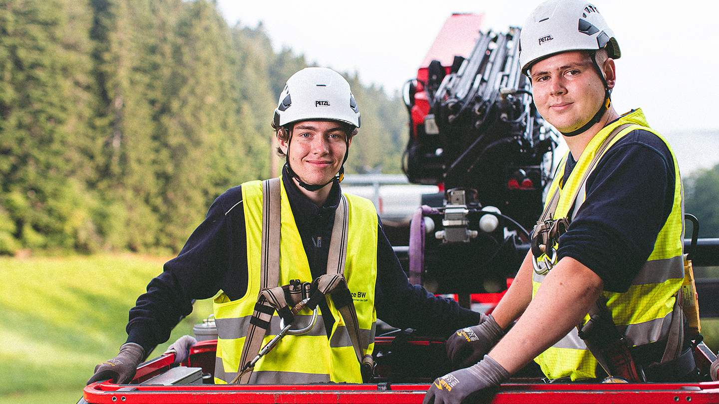 Zwei Monteure mit Sicherheitsausrüstung stehen auf der Hebebühne eines Krans.