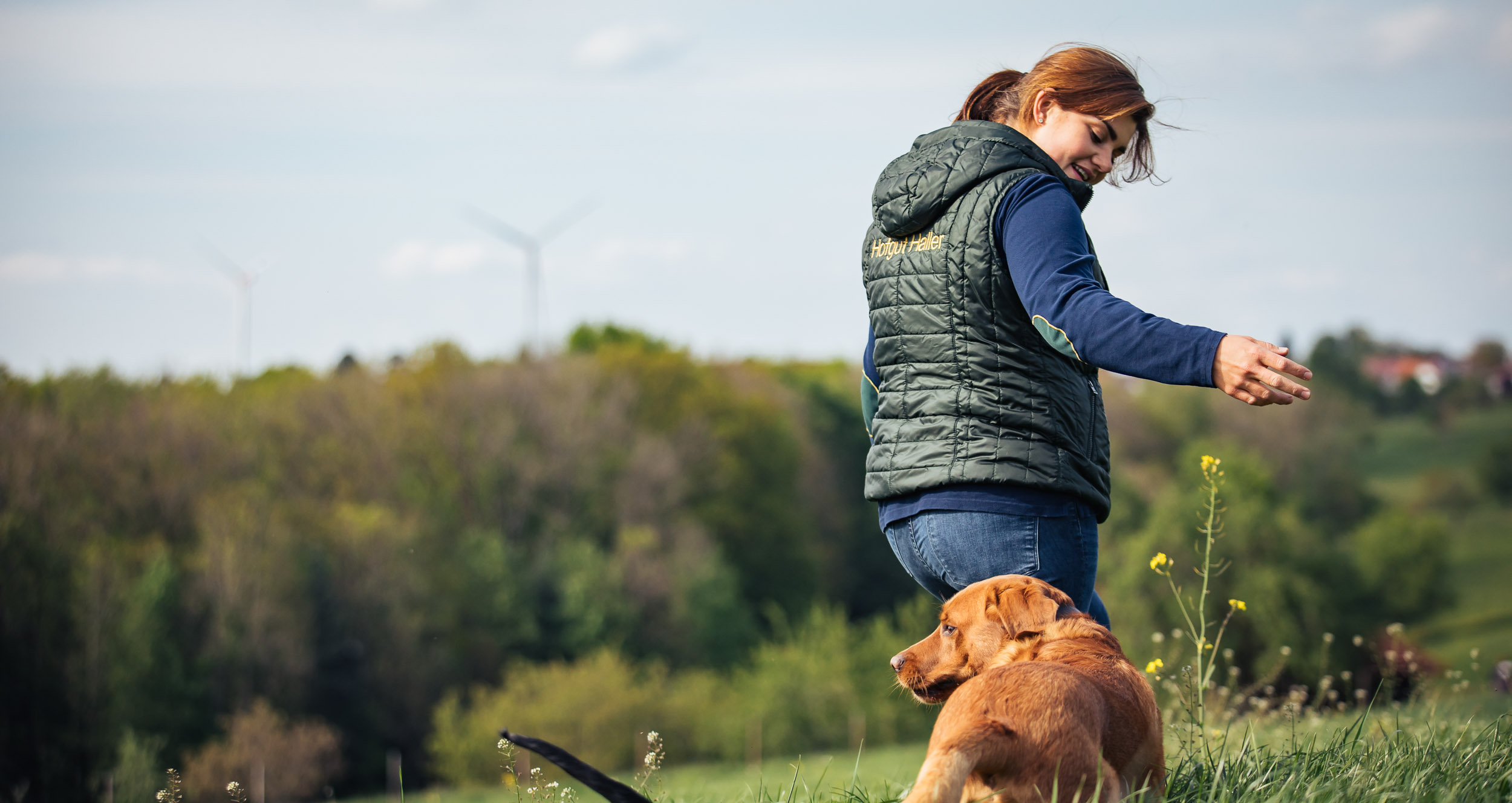 Frau mit Hund auf Wiese.