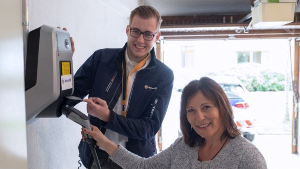 Mann und Frau stehen lächelnd neben einer E-Auto-Wallbox.