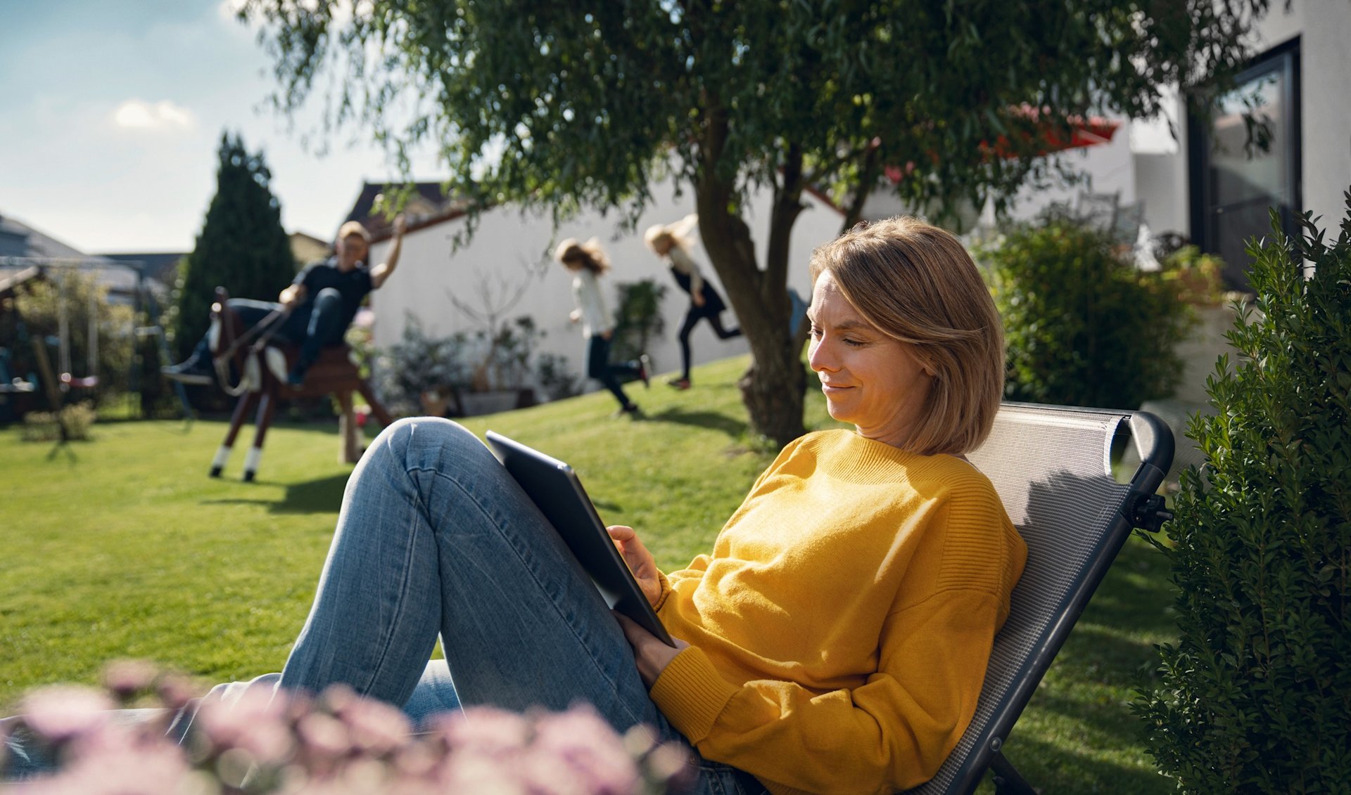 Frau entspannt im Garten, Tablet in der Hand.