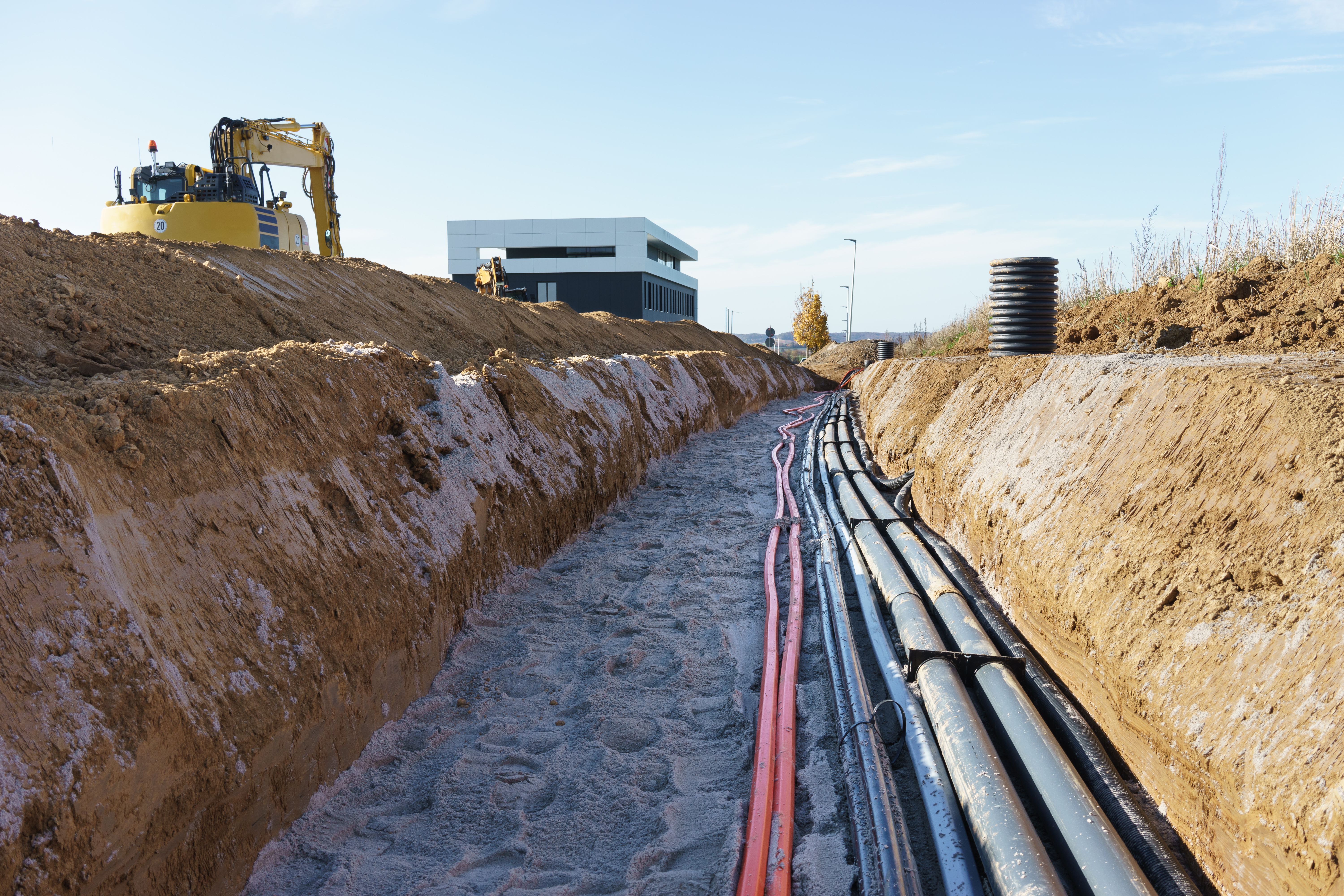 Kabelverlegung im Erdkanal. Bagger im Hintergrund.