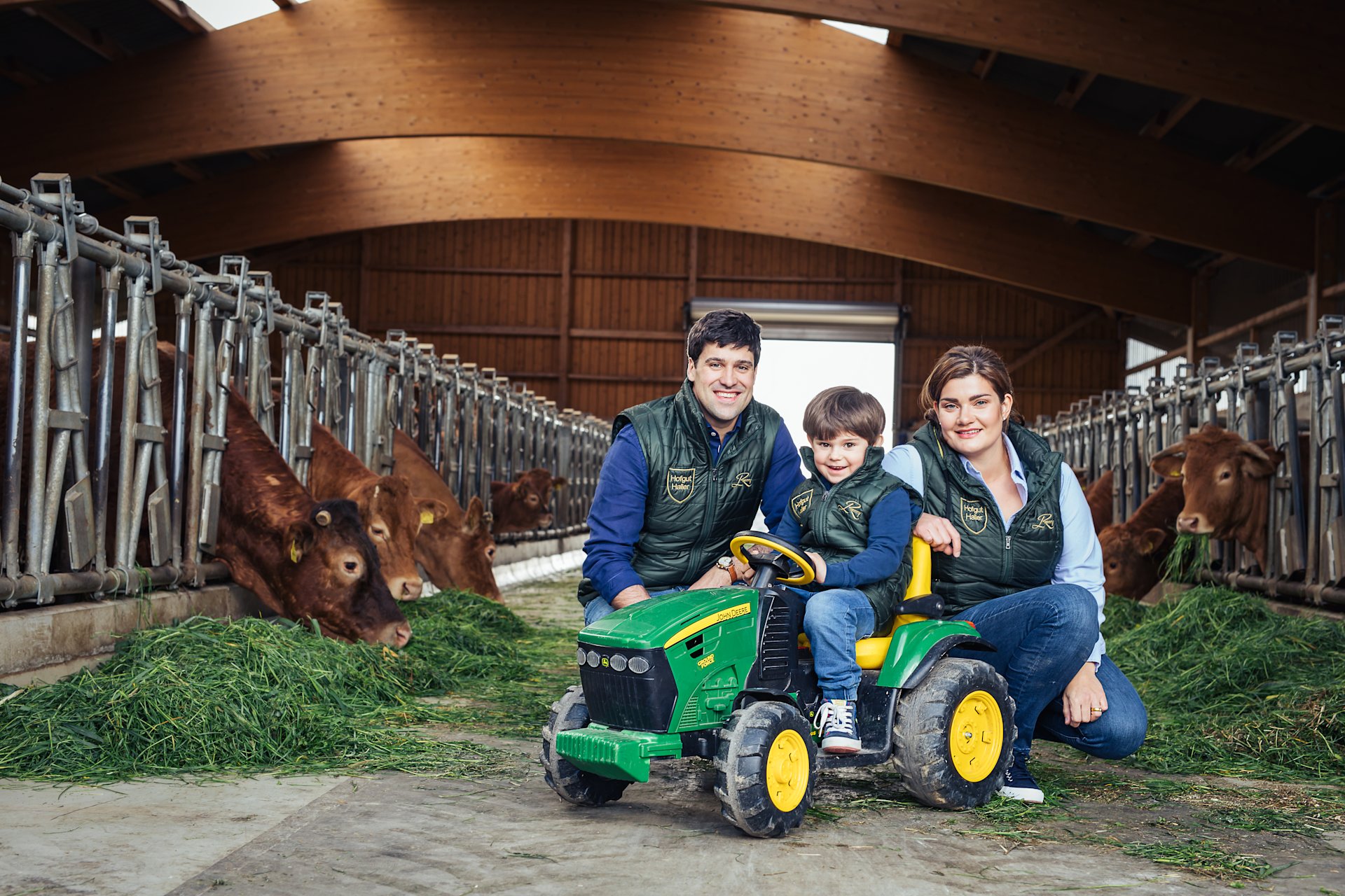 Mann, Frau und Kind auf Bauernhof mit Rindern und Traktor.