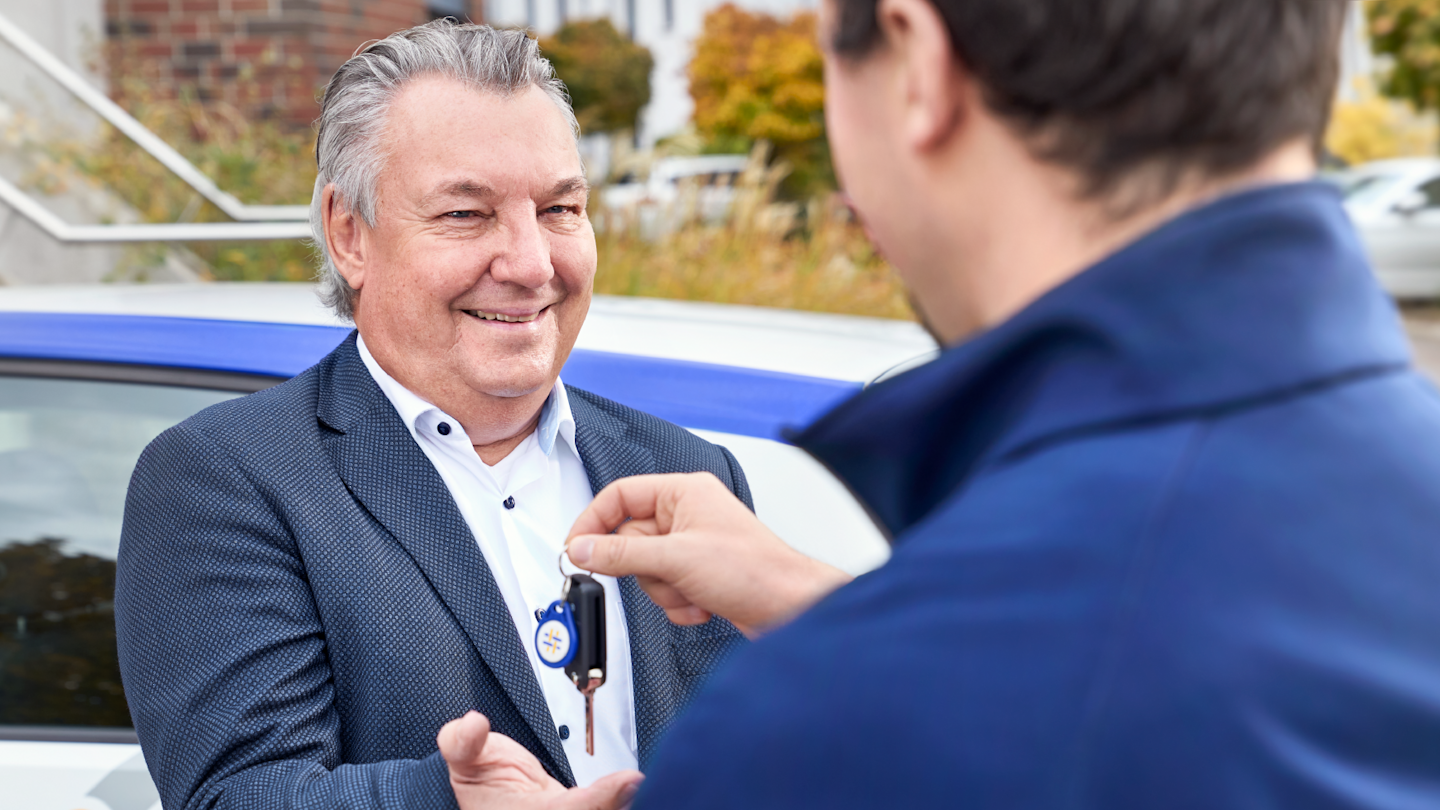 Schlüsselübergabe von zwei Männern vor Auto.