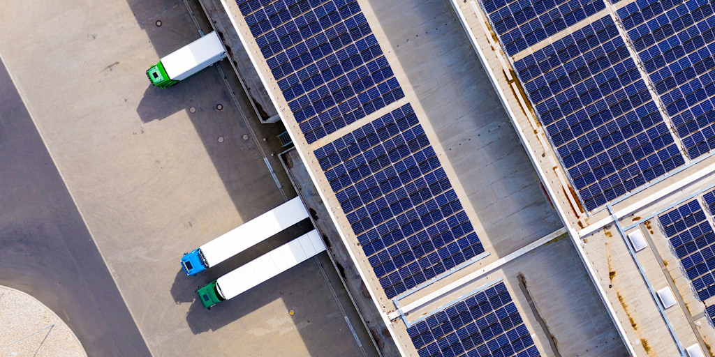 Vogelperspektive eines Logistikdepots mit zu- bzw. abliefernden LKW und Photovoltaik-Anlagen auf den Hallendächern