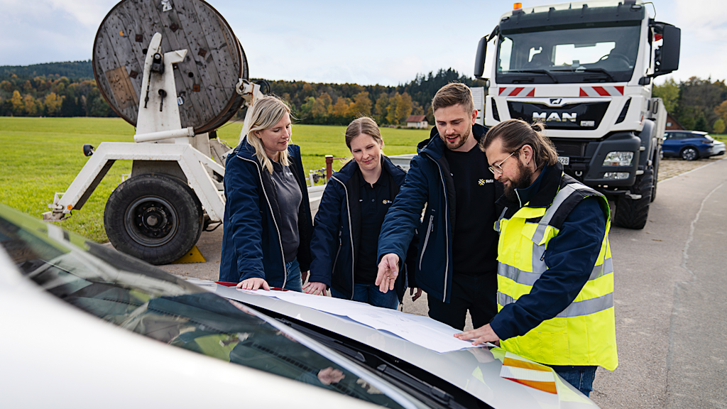 Vier Personen besprechen Pläne, die auf einer Motorhaube liegen.