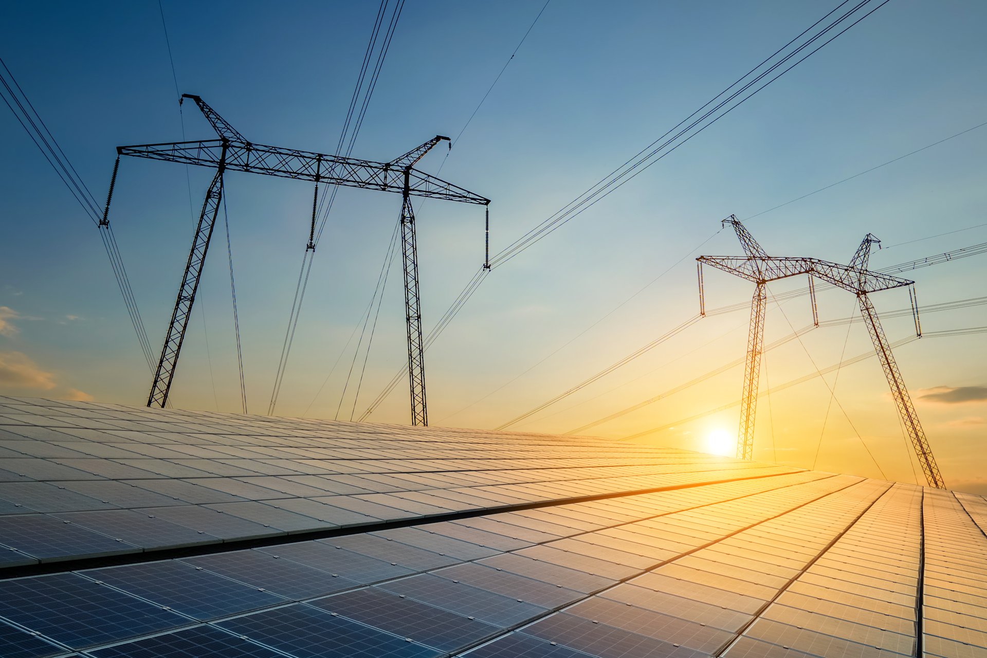 Solarmodule mit Hochspannungsmasten bei Sonnenuntergang.
