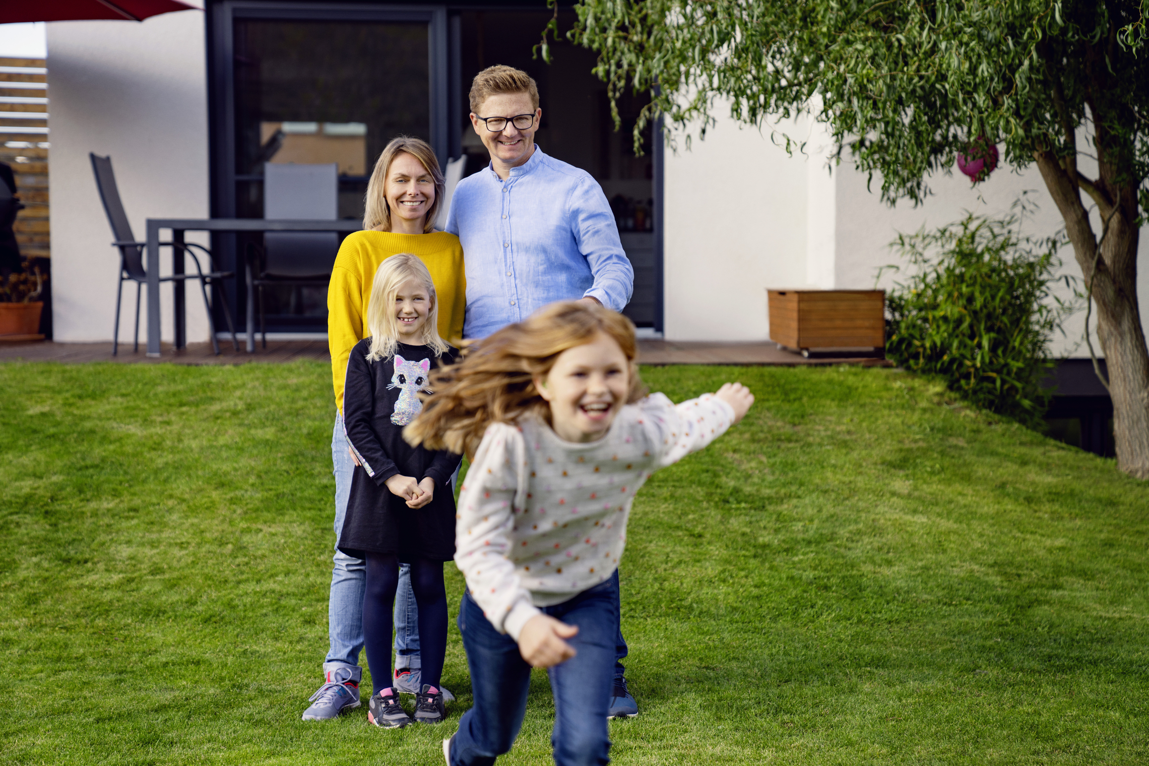Mann, Frau und zwei Mädchen im Garten, Kinder spielen.