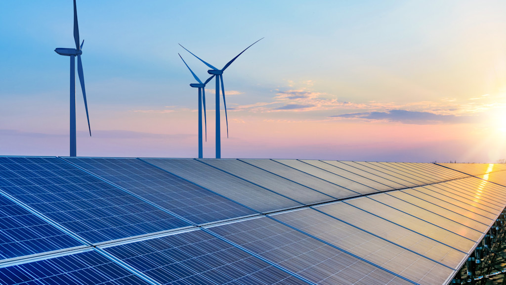 Solarpaneele und drei Windräder bei Sonnenuntergang.