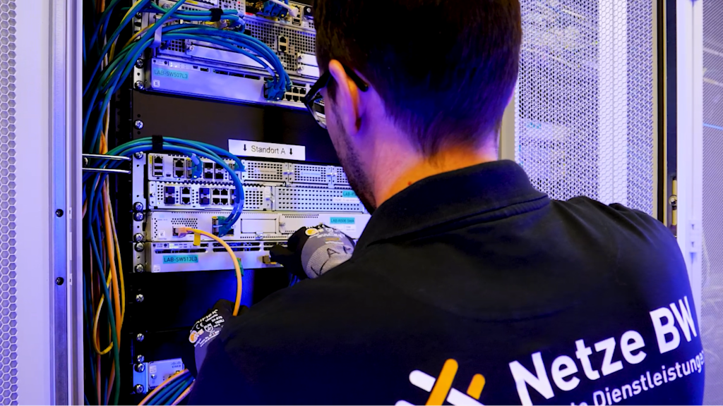 Netze BW Mitarbeiter vor einem Serverschrank mit Kontrollbildschirmen