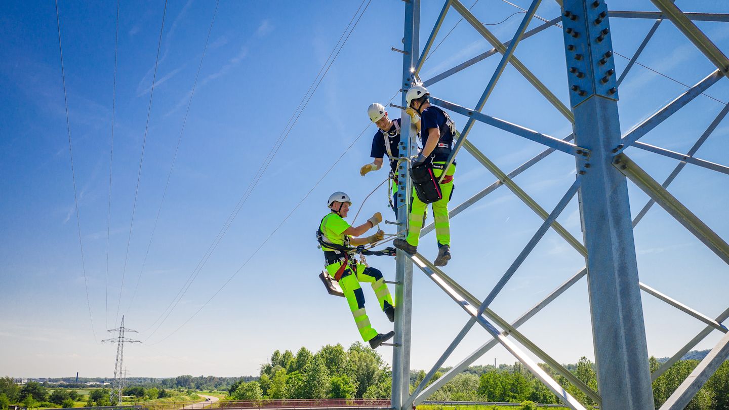 Drei Monteure arbeiten an einem Hochspannungsmast.