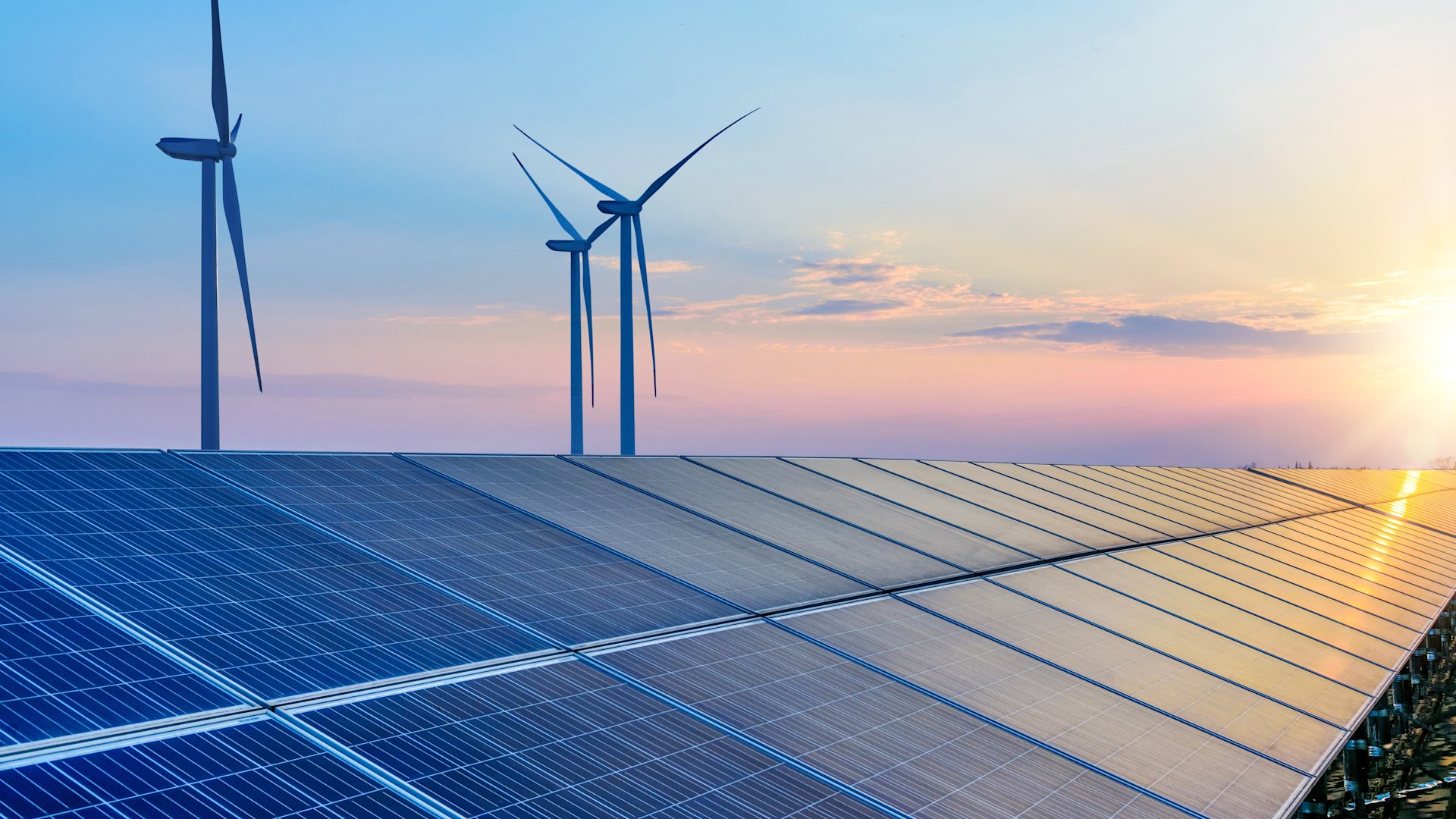 Solarpaneele und drei Windräder bei Sonnenuntergang.