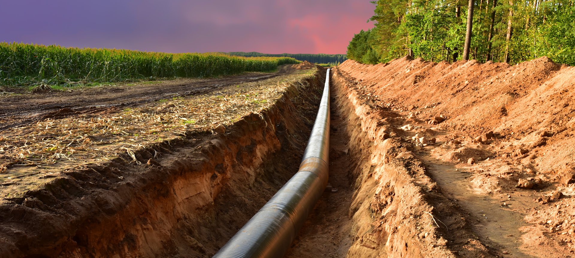 Rohrleitung in Graben, neben Feld und Wald.