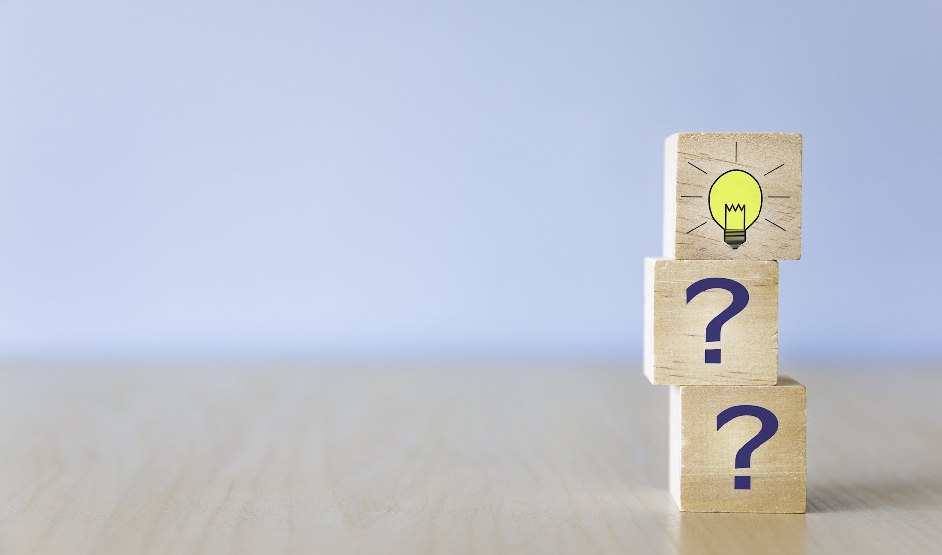 Drei gestapelte Holzwürfel mit Fragezeichen und Glühbirne darauf.