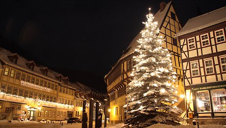 Weihnachtlich beleuchteter Tannenbaum im Schnee vor Fachwerkhäusern.