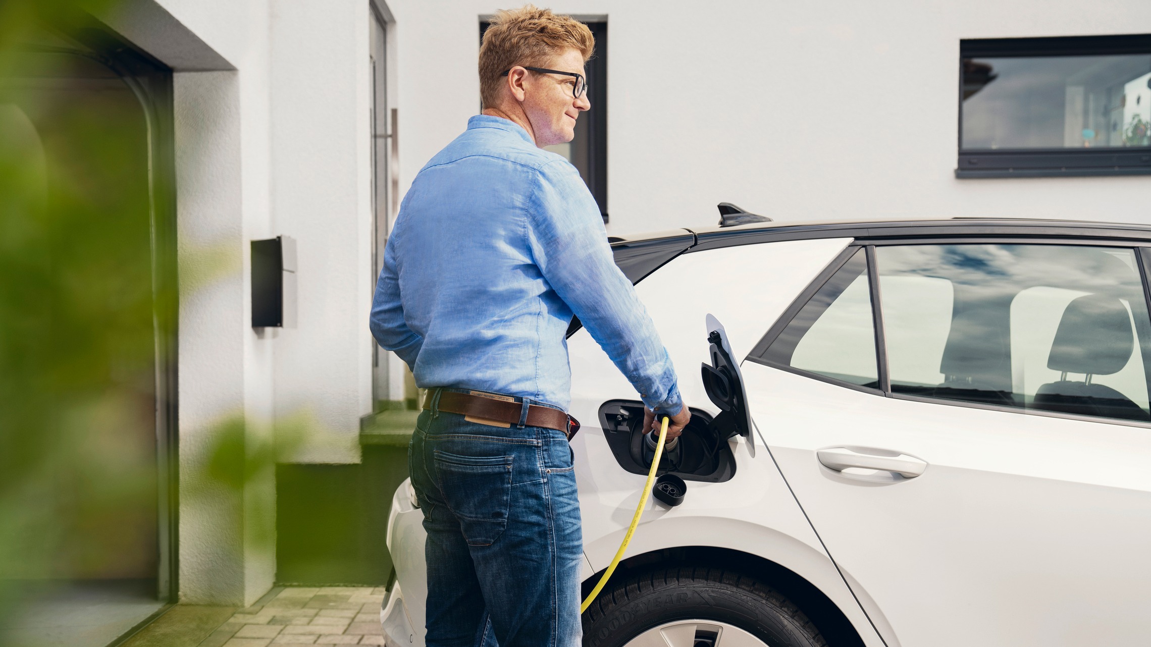 Lächelnder Mann lädt sein E-Auto mit dem Ladekabel.